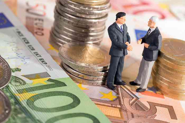 Zwei kleine Figuren stehend auf Geldscheine umringt von Münzen  - © PhotographyByMK - stock.adobe.com